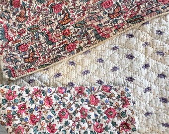 May include: A patchwork quilt with a floral pattern in shades of pink, green, and white. The quilt is made of different fabrics and has a quilted texture.