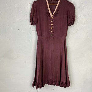 May include: A maroon silk dress with a pink lace trim around the neckline and short sleeves. The dress has a button-up front and a ruffled hem.