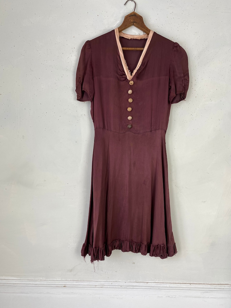 May include: A maroon silk dress with a pink lace trim around the neckline and short sleeves. The dress has a button-up front and a ruffled hem.