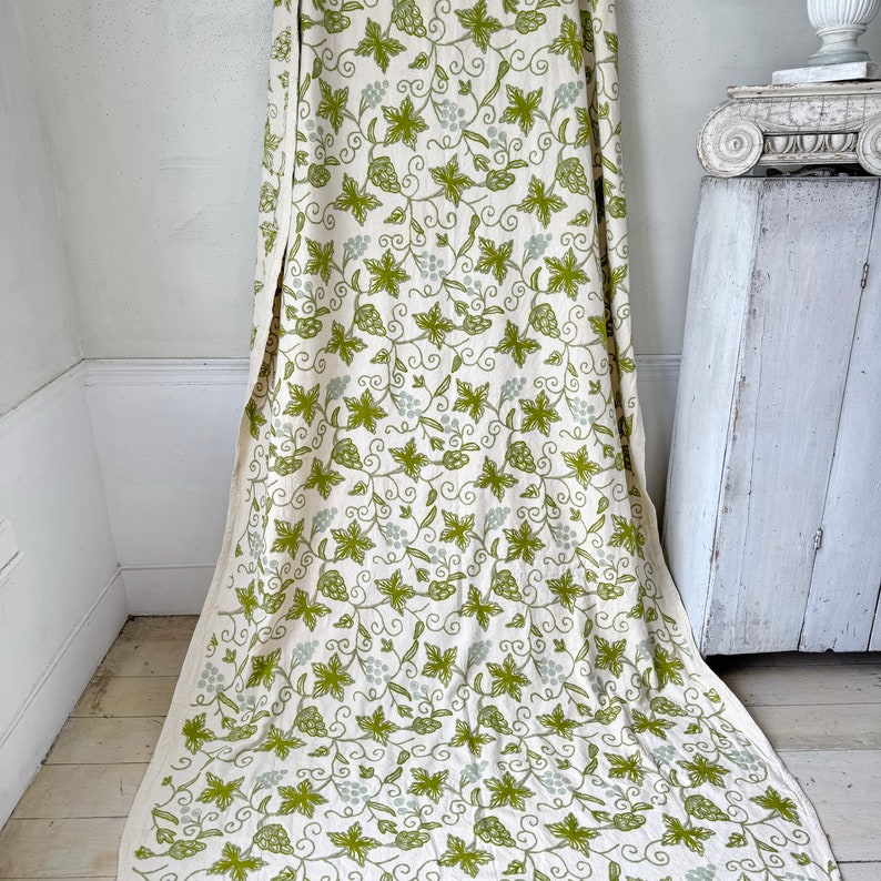 May include: White fabric with a green and gray grapevine pattern. The fabric is draped over a white surface.