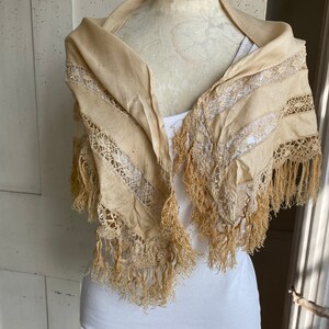 May include: A cream-colored lace shawl with fringe trim. The shawl is displayed on a white mannequin.