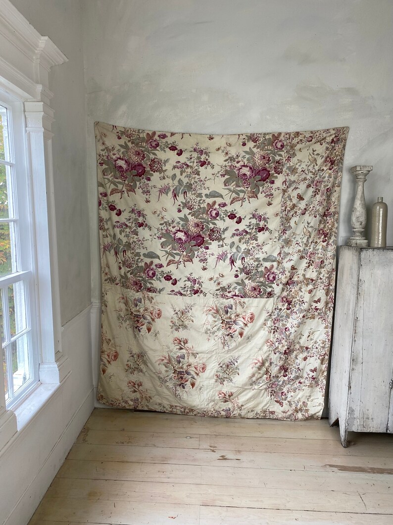 Puede incluir: Un gran panel de tela con estampado floral en tonos rosa, blanco y verde. La tela est&aacute; colgada en una pared en una habitaci&oacute;n con paredes pintadas de blanco y suelo de madera.