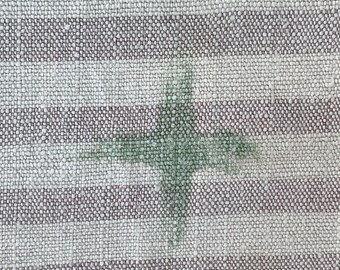 Puede incluir: Primer plano de una tela rayada blanca y gris con un diseño en forma de cruz verde en el centro.