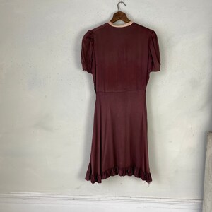 May include: A maroon wrap dress with short sleeves and a ruffled hem. The dress has a pink trim around the neckline.