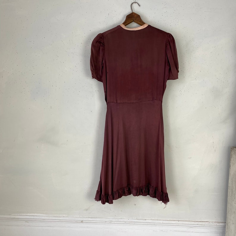 May include: A maroon wrap dress with short sleeves and a ruffled hem. The dress has a pink trim around the neckline.