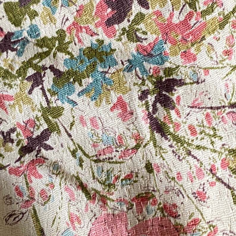 May include: Close-up of a white fabric with a floral pattern. The pattern features pink, blue, and green flowers on a white background.