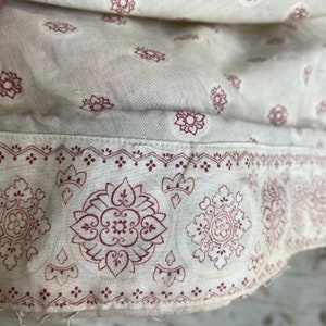 K&ouml;nnte beinhalten: Nahaufnahme eines wei&szlig;en Stoffes mit einem rot-wei&szlig;en Muster. Der Stoff hat eine subtile Textur und ein zartes Blumenmuster.