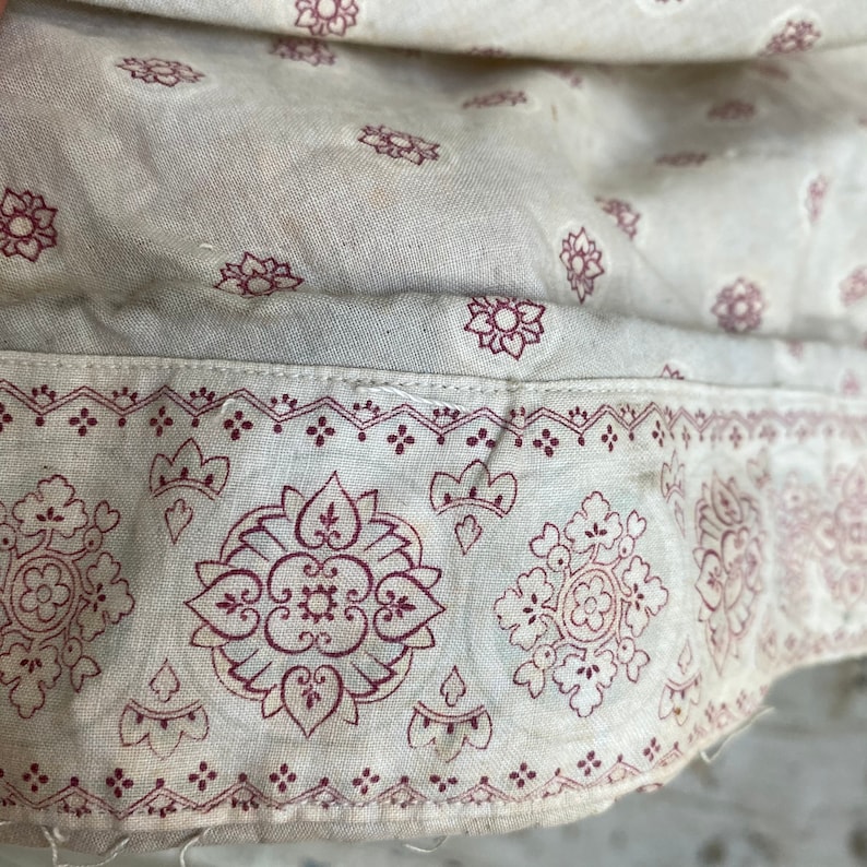 K&ouml;nnte beinhalten: Nahaufnahme eines wei&szlig;en Stoffes mit einem rot-wei&szlig;en Muster. Der Stoff hat eine subtile Textur und ein zartes Blumenmuster.