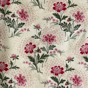 May include: A white fabric with a repeating pattern of pink flowers and green leaves. The background is a light cream color with a subtle speckled pattern.