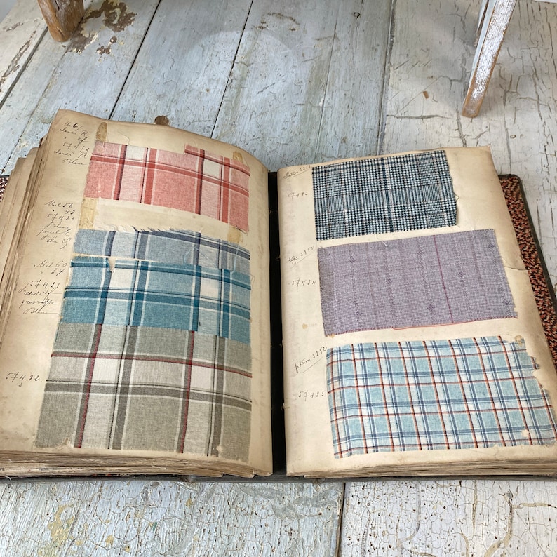 May include: An open book with fabric swatches. The swatches are different patterns of plaid and gingham in blue, red, and white. The book has handwritten numbers and text on the pages.