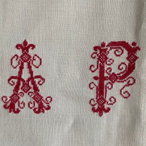 May include: A white linen fabric with red embroidered letters "A" and "P" in a decorative font.