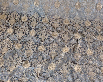 May include: A close-up of a blue and gold fabric with a repeating floral pattern. The fabric has a textured, almost quilted appearance.