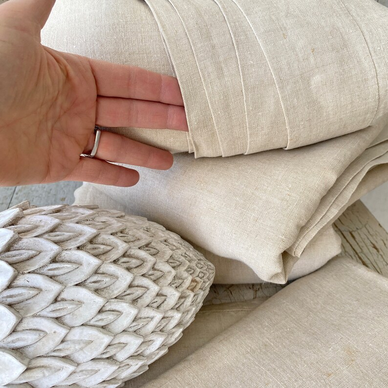 May include: A stack of natural linen fabric, folded and layered, with a white decorative object in the foreground.