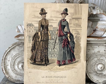 May include: A vintage fashion illustration from La Mode Française, a French fashion magazine, featuring two women in elaborate dresses and hats. The illustration is printed on paper with a textured surface.