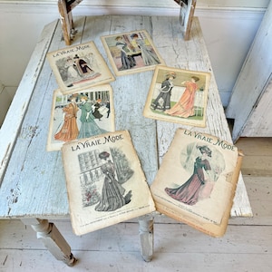May include: A collection of vintage French fashion magazines, "La Vraie Mode", featuring illustrations of women in various styles of clothing. The magazines are printed on yellowed paper with black text and illustrations.