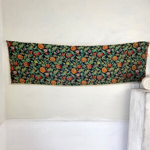 May include: A black tapestry with a floral pattern in shades of orange, red, green, and yellow. The tapestry has a fringe border.