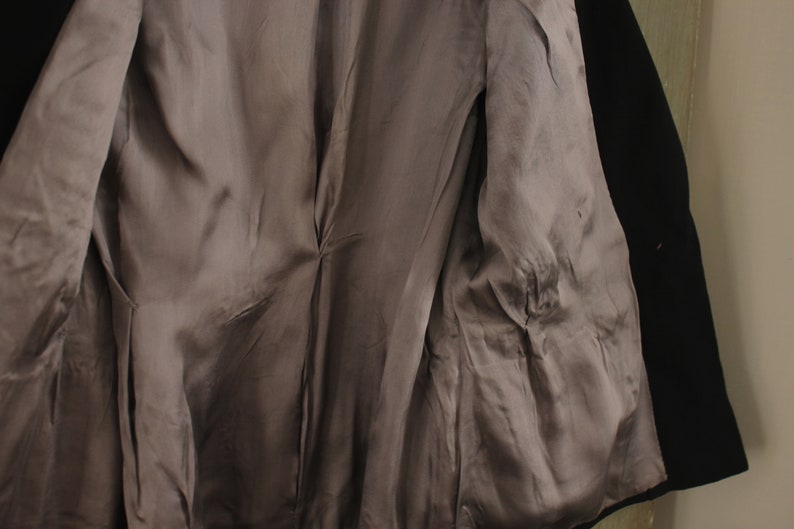 May include: A black blazer with a gray satin lining. The blazer has a double-breasted closure and a single button on the right side.