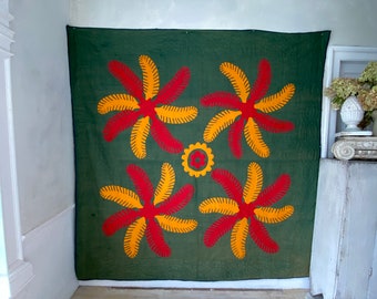 May include: A green fabric wall hanging with a repeating pattern of red and yellow stylized flowers. The flowers are arranged in a symmetrical pattern.