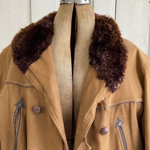 May include: A brown canvas jacket with a brown faux fur collar. The jacket has a double breasted closure and two pockets on the front.
