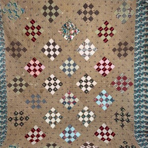 Puede incluir: Una colcha marrón con un diseño de patchwork. La colcha está hecha de cuadrados de diferentes telas, incluyendo marrón, blanco, rojo y azul. La colcha está bordeada con un borde verde y blanco.