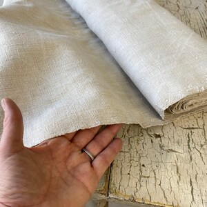 May include: A roll of natural linen fabric with a slightly textured surface. The fabric is folded in half and the edges are frayed.