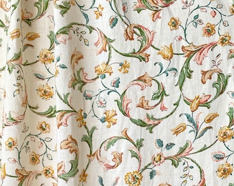 Puede incluir: Una tela blanca con un patrón repetitivo de diseños florales verdes, rosas y amarillos. El patrón presenta intrincados remolinos y hojas.