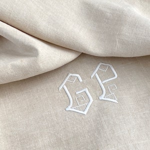 May include: A close-up of a white linen fabric with the embroidered initials "GP" in a decorative font.
