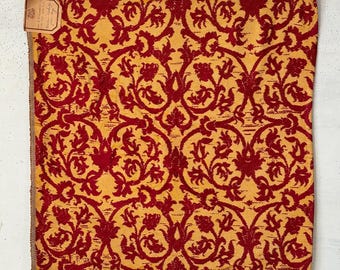 May include: A red and gold fabric swatch with a floral pattern. The fabric has a textured, almost velvet-like appearance.