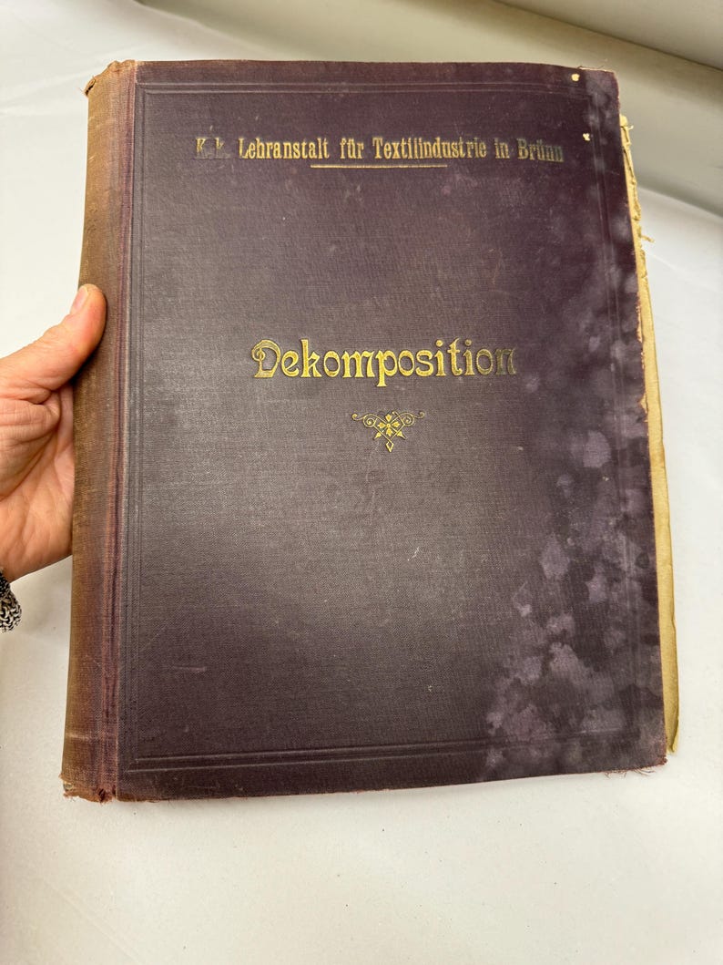 May include: A dark brown book with gold lettering on the cover. The title is "Dekomposition" and the book is from the K.k. Lehranstalt fur Textilindustrie in Brunn.