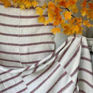 May include: A white and red striped fabric with a woven texture. The fabric is folded and draped over a surface.
