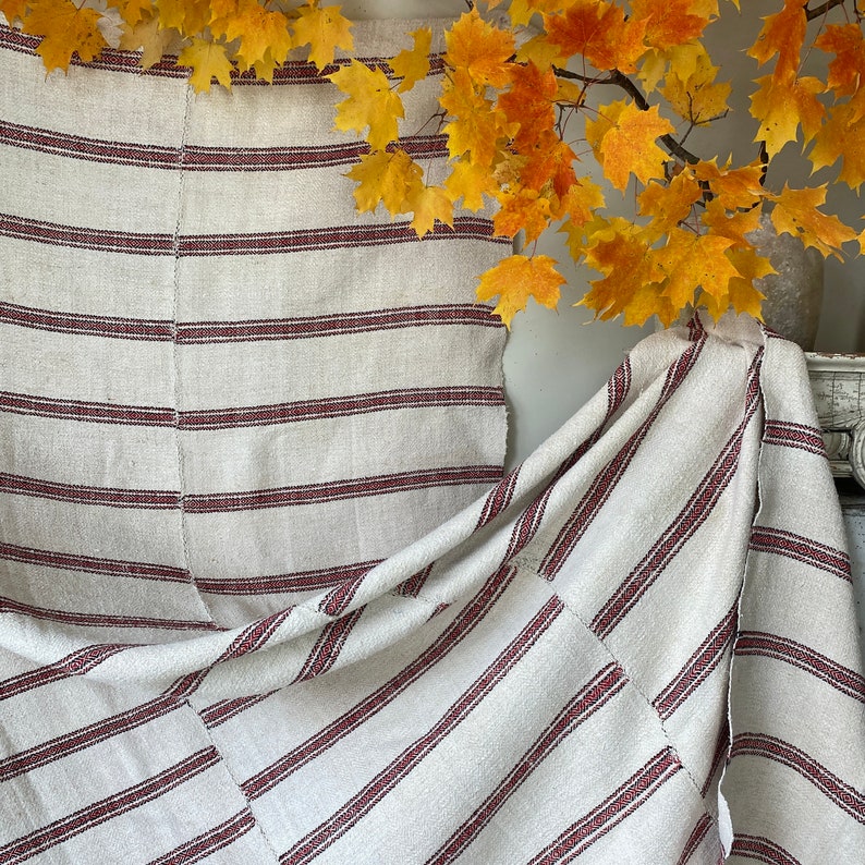 May include: A white and red striped fabric with a woven texture. The fabric is folded and draped over a surface.