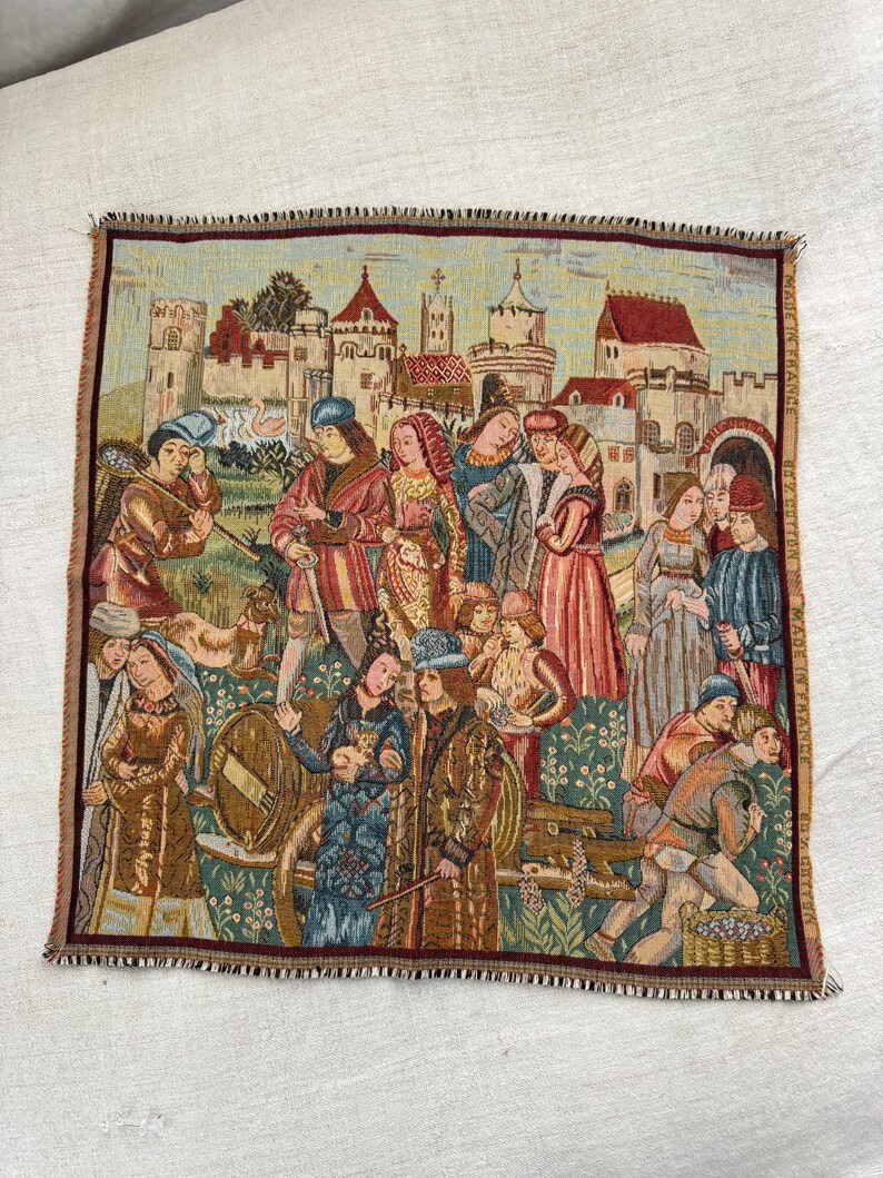 May include: Tapestry featuring a medieval scene with figures in period clothing, a castle backdrop, and a border with a frayed edge. The tapestry is made in France.