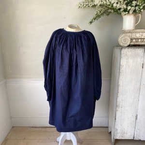 May include: A navy blue, loose-fitting, gathered-neck dress with long sleeves. The dress is made of a soft, textured fabric and has a relaxed, comfortable fit.
