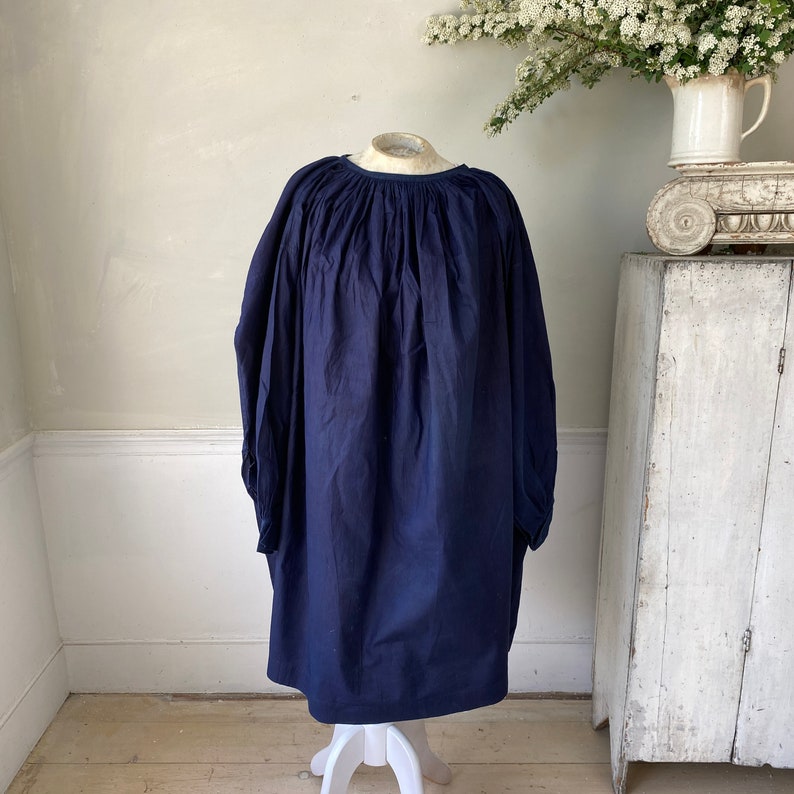 May include: A navy blue, loose-fitting, gathered-neck dress with long sleeves. The dress is made of a soft, textured fabric and has a relaxed, comfortable fit.