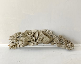 Puede incluir: Un diseño floral de madera pintado de blanco con detalles intrincados. El diseño presenta un grupo de flores y hojas talladas, creando un elemento decorativo para un hogar o un mueble.