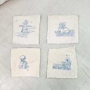 May include: Four embroidered squares with blue thread on a white background. The squares feature a girl on the beach, two girls hugging on a brick wall, a girl blowing dandelion seeds, and a train.