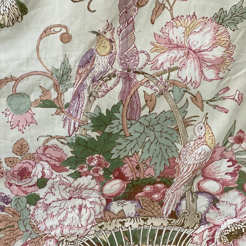 Puede incluir: Una tela blanca con un patr&oacute;n floral que presenta flores rosas, hojas verdes y dos p&aacute;jaros. Los p&aacute;jaros est&aacute;n posados en una rama con un dise&ntilde;o a rayas marrones y blancas.