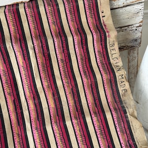 May include: A piece of vintage paper with a striped pattern in black, pink, and gold. The paper has a beige background and the text "BELGIAN MADE" is visible on the right edge. The design features vertical stripes.