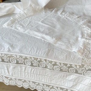 May include: White cotton bed sheet with delicate lace trim and embroidered floral designs. The sheet has a scalloped edge and a small pillowcase with a similar design.