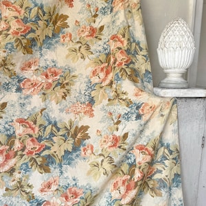 May include: A cream-colored fabric with a floral pattern featuring pink, blue, and green flowers. The fabric has a vintage feel and is perfect for upholstery or curtains.