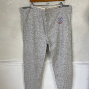 Pode incluir: Cal&ccedil;as de moletom cinzas com c&oacute;s branco e fechamento com bot&atilde;o. As cal&ccedil;as de moletom t&ecirc;m um logotipo circular na perna direita que diz "Champion" e "Athletic Wear".