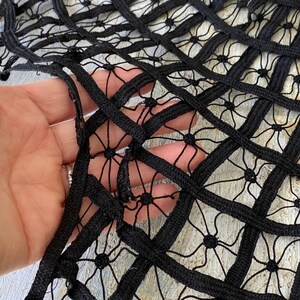 May include: Black lace fabric with a geometric pattern of squares and circles. The fabric is made of a thick, woven material and has a slightly textured surface.
