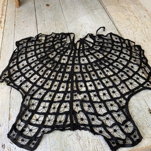 May include: Black lace doily with a circular design. The lace is delicate and intricate, with a spiderweb-like pattern.
