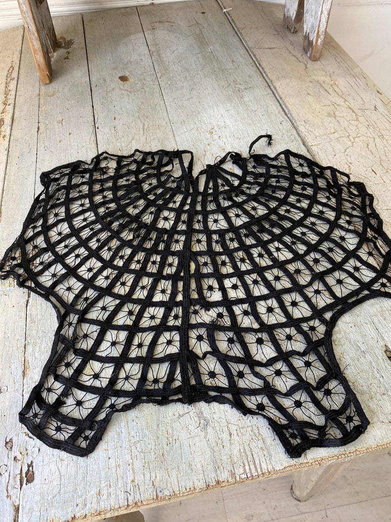 May include: Black lace doily with a circular design. The lace is delicate and intricate, with a spiderweb-like pattern.