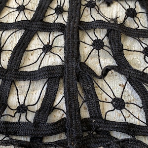 May include: Close-up of black braided rope woven into a geometric pattern with a white background. The rope is woven into a grid pattern with a series of circles in the center of each square.