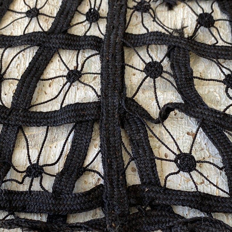 May include: Close-up of black braided rope woven into a geometric pattern with a white background. The rope is woven into a grid pattern with a series of circles in the center of each square.