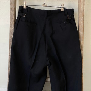 May include: Black pleated pants with a single back pocket and belt loops.