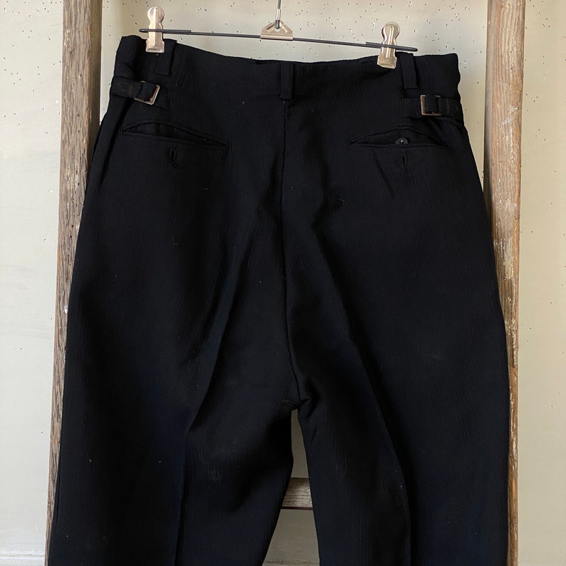 May include: Black pleated pants with a single back pocket and belt loops.