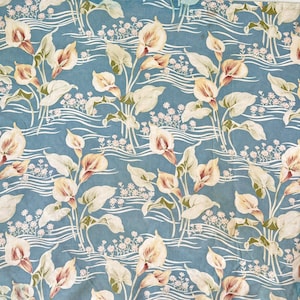 May include: A blue fabric with a repeating pattern of white and cream calla lilies with brown accents. The background has a wavy pattern.