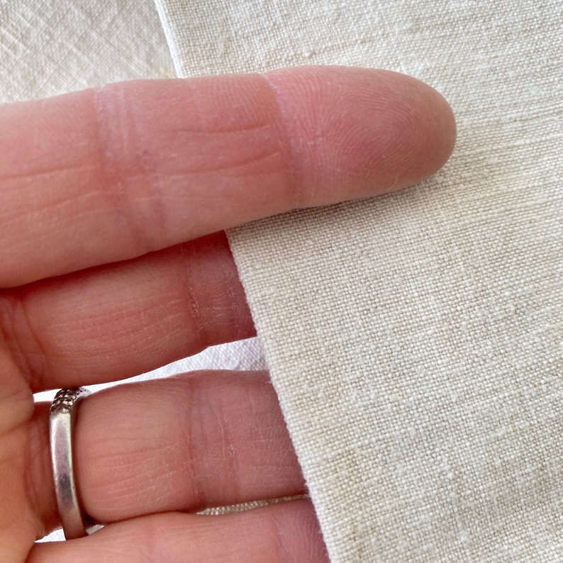 May include: Close-up of a natural linen fabric with a slightly textured surface. The fabric is a light beige color.